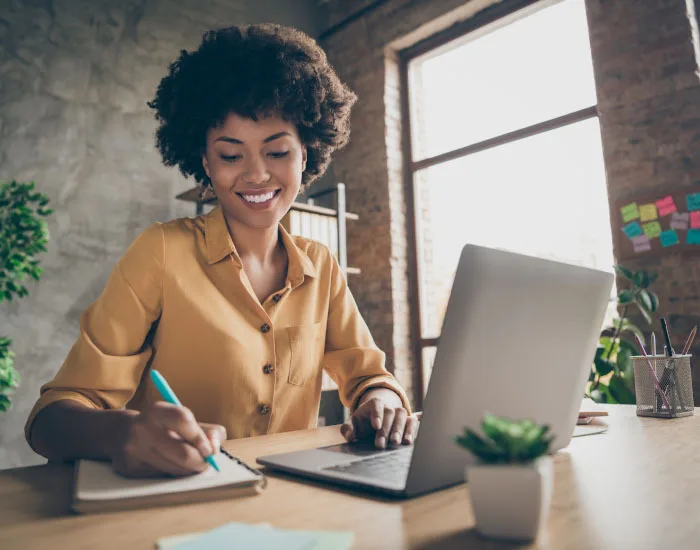 Femme devant son ordinateur portable écrivant sur un cahier